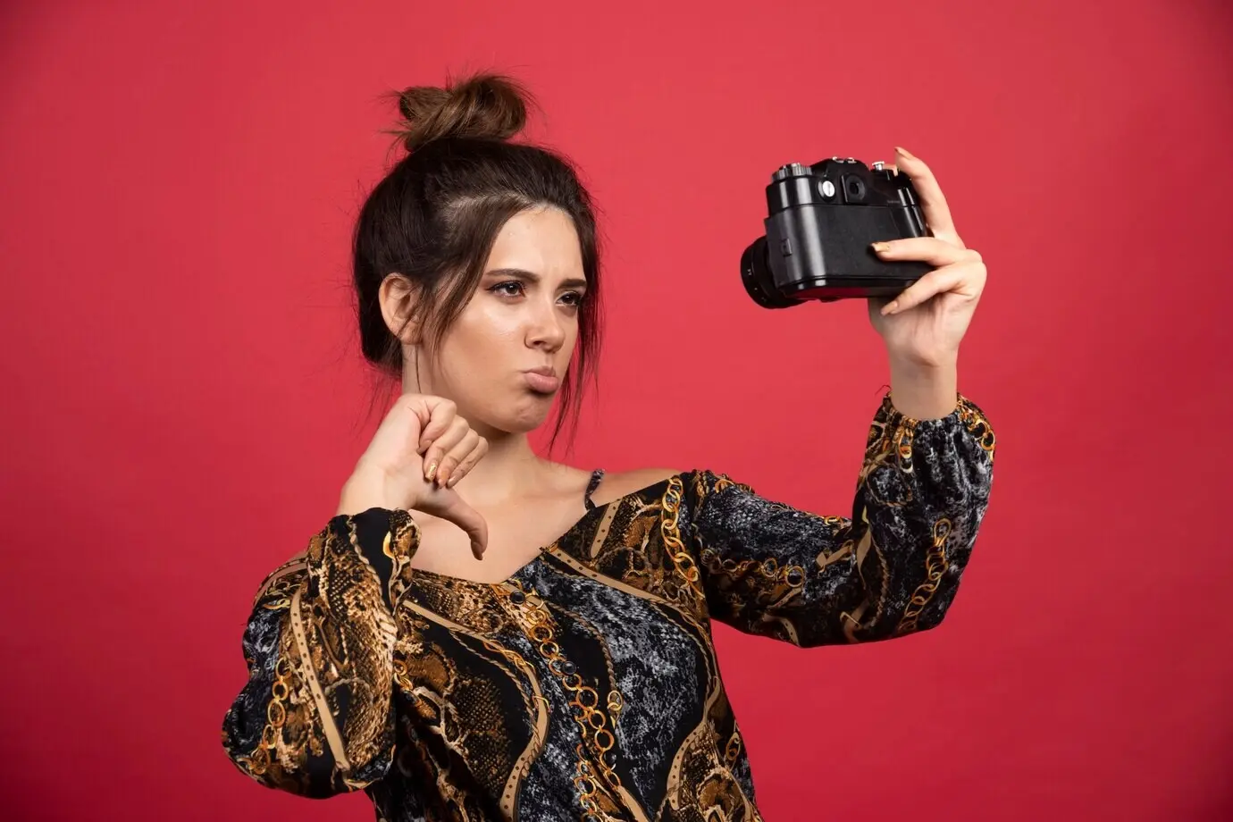 Ein brünettes Mädchen hält eine professionelle DSLR-Kamera und macht ihre enttäuschten Selfies.